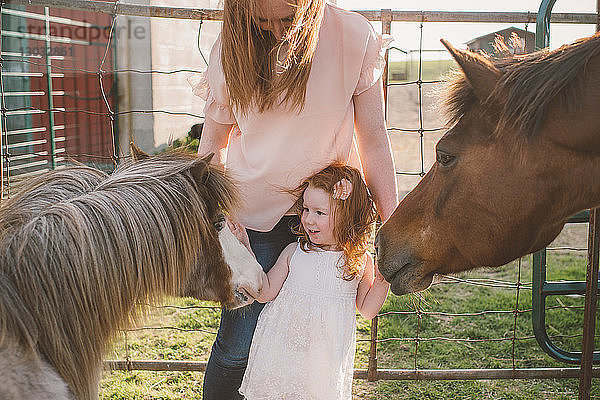 Mutter und Tochter streicheln Pony auf dem Bauernhof