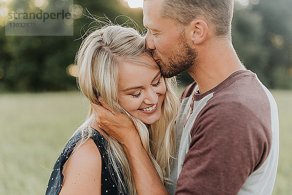 Romantischer Mann küsst im Feld seine Freundin auf die Stirn