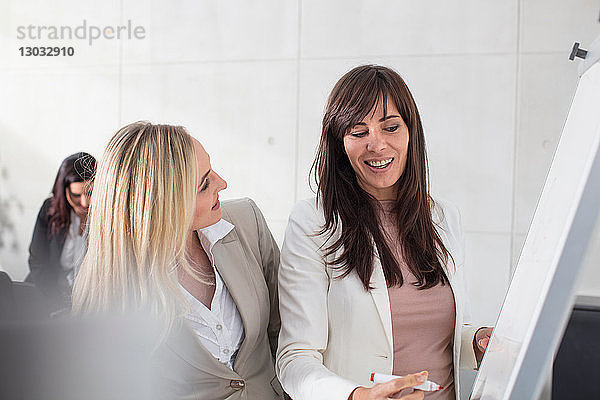 Geschäftsfrauen im Gespräch mit Kollegen und Schreiben an der Tafel im Büro