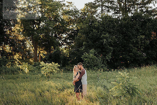 Romantischer Mann umarmt Freundin im Feld aus langem Gras
