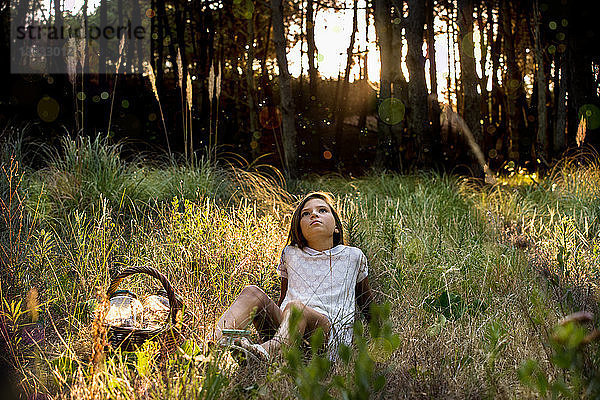 Mädchen mit Picknickkorb im sonnenbeschienenen Wald liegend und nach oben blickend
