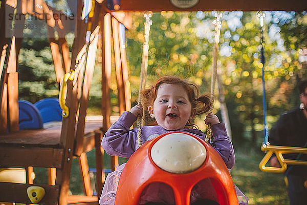 Mädchen mit roten Haaren auf Spielplatzschaukel schwingend  Portrait