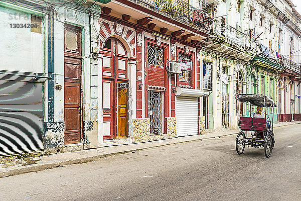 Eine alte Fahrradrikscha  die an schöner lokaler Architektur in Havanna  Kuba  Westindien  Karibik vorbeifährt