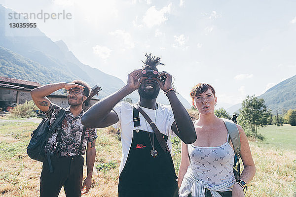 Drei junge Wanderfreunde schauen durch ein Fernglas aus der Feldlandschaft auf  Primaluna  Trentino-Südtirol  Italien