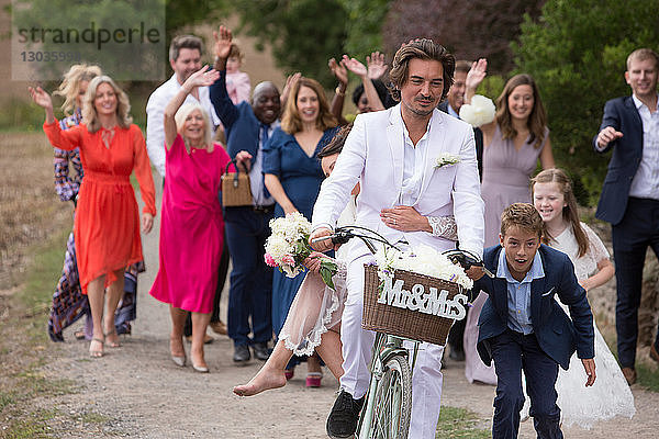 Hochzeitsgäste winken Brautpaare auf Fahrrädern ab