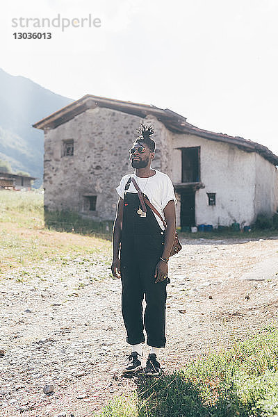 Kühler junger Mann in Latzhose beim Bauernhaus  Porträt  Primaluna  Trentino-Südtirol  Italien