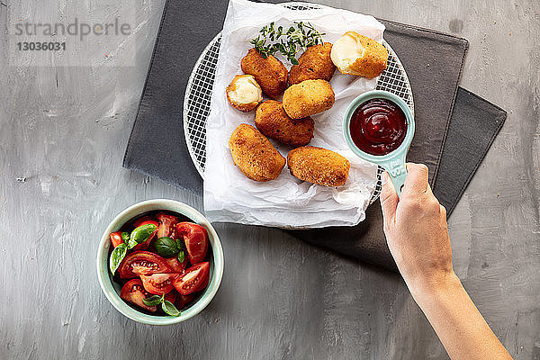 Tomatensauce mit Kartoffelkroketten auf Teller legen  Blick von oben auf die Hand