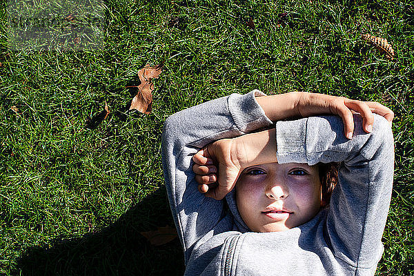 Junge auf Gras blockiert Sonnenlicht mit Armen