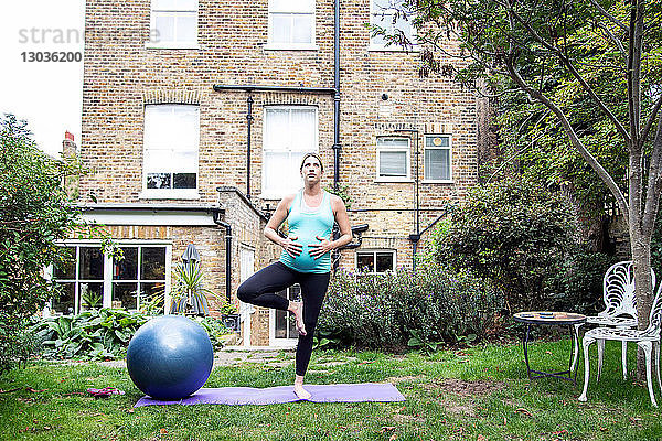 Schwangere Frau im mittleren Erwachsenenalter übt Yoga-Baum-Pose im Garten