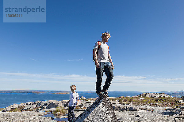 Junge und Vater schauen von der Spitze einer Felsformation über die Landschaft hinaus  Aure  More og Romsdal  Norwegen
