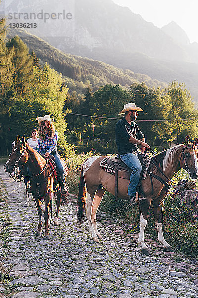 Erwachsene Freunde beim Reiten auf ländlicher Kopfsteinpflasterstraße  Primaluna  Trentino-Südtirol  Italien