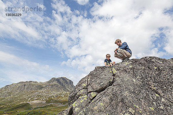Junge und Vater kauern auf einer Felsformation  Blick aus niedrigem Winkel  Oppland  Nord-Trondelag  Norwegen
