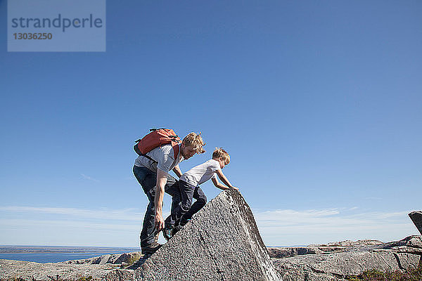 Junge und Vater klettern an einer Felsformation über dem Meeresarm  Aure  More og Romsdal  Norwegen