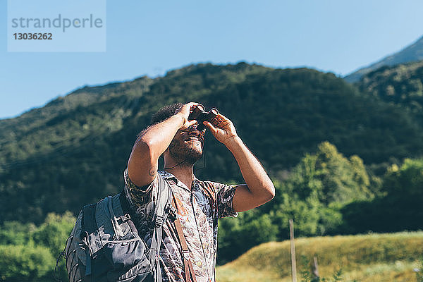 Junger männlicher Wanderer  der durch ein Fernglas nach oben schaut  Primaluna  Trentino-Südtirol  Italien