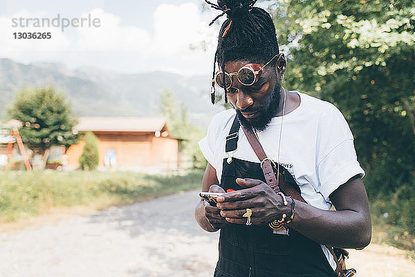 Cooler junger Mann auf ländlichem Feldweg mit Blick auf Smartphone  Primaluna  Trentino-Südtirol  Italien