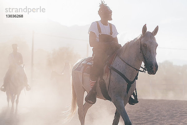 Kühler junger Mann reitet Pferd in staubiger ländlicher Reithalle