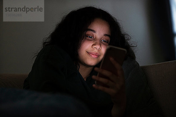 Teenager-Mädchen sitzt im Dunkeln auf dem Sofa und liest Textnachrichten