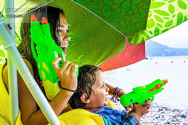 Frau und Junge spielen mit Wasserpistolen am Strand