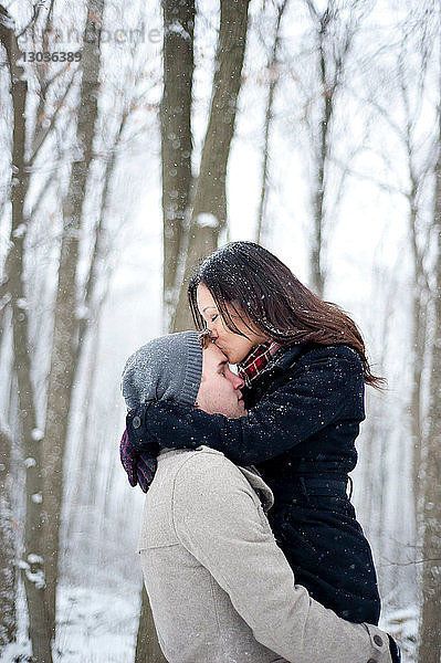 Romantische junge Frau küsst in verschneitem Wald die Stirn ihres Freundes  Ontario  Kanada