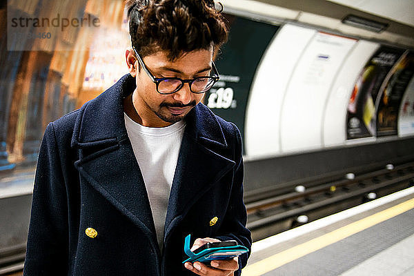 Geschäftsmann mit Smartphone auf dem Bahnsteig einer U-Bahn-Station  London  Großbritannien