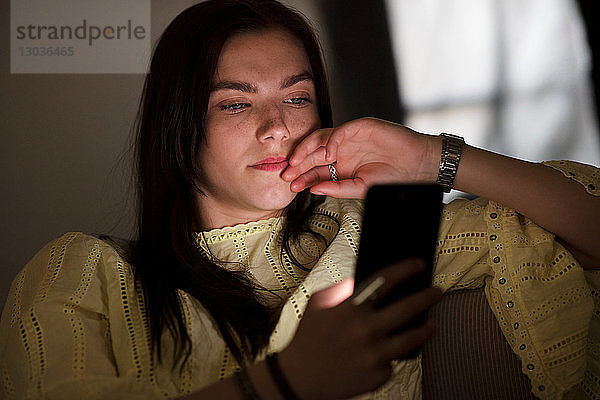 Teenager-Mädchen sitzt im Dunkeln auf dem Sofa und liest Textnachrichten
