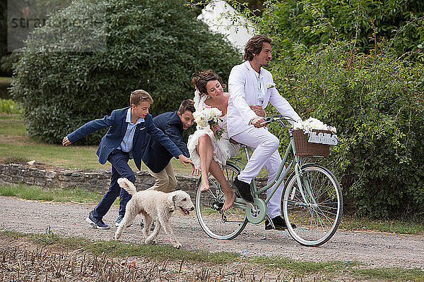 Junge Hochzeitsgäste rennen Neuvermählten auf Fahrrädern hinterher