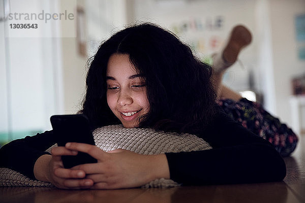 Teenager-Mädchen liegt auf einem Kissen auf dem Boden und liest eine Textnachricht