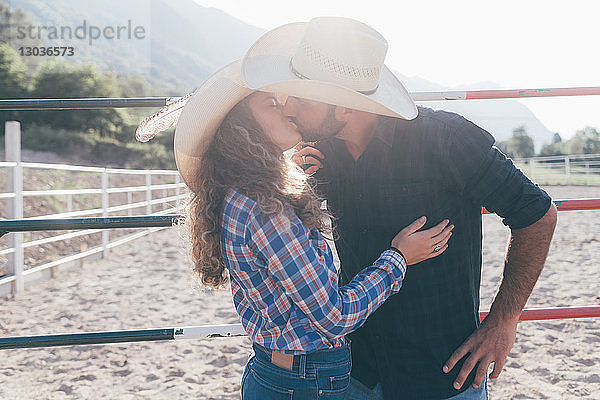 Junges Cowgirl und Freund küssen sich in ländlicher Reitarena
