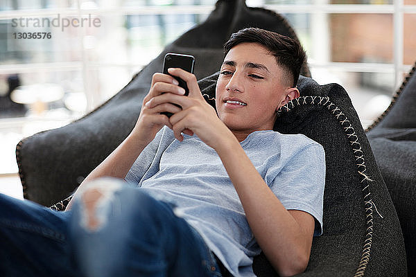 Teenager-Junge liegt auf Sitzsack und liest Textnachricht auf Handy