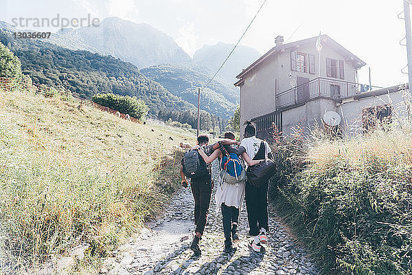 Junge erwachsene Wanderfreunde mit den Armen umeinander auf der Landstraße  Primaluna  Trentino-Südtirol  Italien