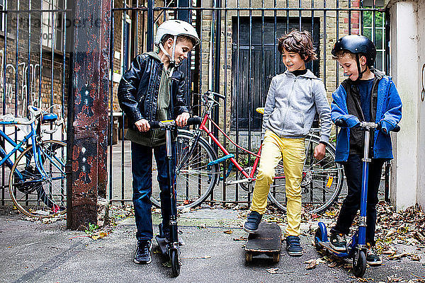 Jungen fahren Roller und Skateboard  Fahrräder im Hintergrund