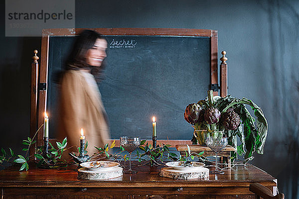 Junge Frau bewegt sich an einem alten Esstisch mit Kerzen und einer Schale mit Artischocken