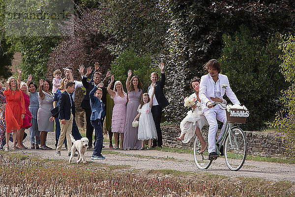 Hochzeitsgäste winken dem Brautpaar auf Fahrrädern