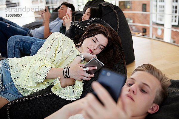 Schulfreunde liegen auf Sitzsäcken und schreiben in der Schule SMS