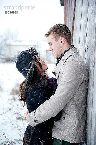 Junges Paar umarmt sich an Hütte im Schnee