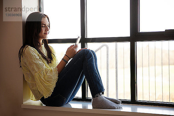 Teenagerin liest Textnachricht auf Handy durch Glasfenster