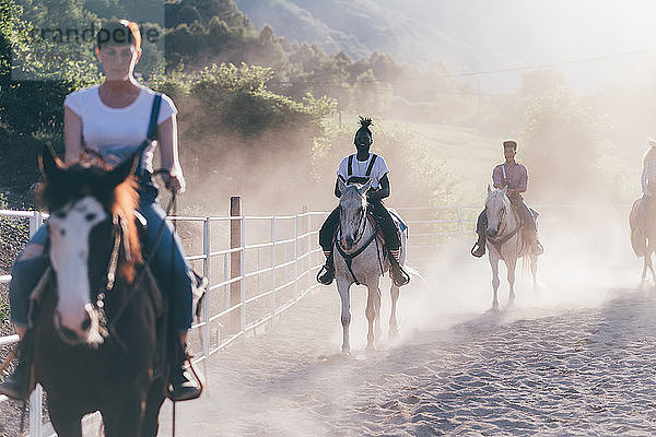 Junge Erwachsene reiten auf Pferden in staubiger ländlicher Reithalle