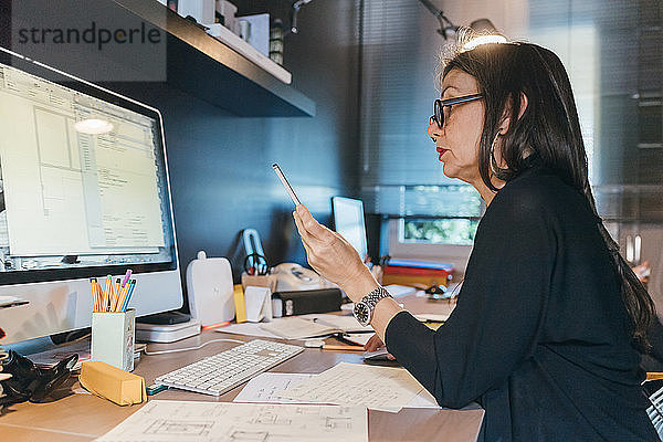 Frau benutzt Handy am Schreibtisch