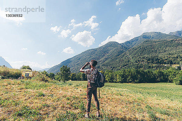 Junger männlicher Wanderer  der durch ein Fernglas in Richtung Berge blickt  Primaluna  Trentino-Südtirol  Italien