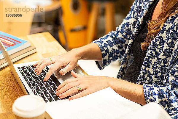 Schwangere Frau im mittleren Erwachsenenalter beim Tippen am Laptop am Küchentisch  abgeschnitten