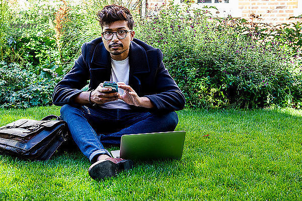 Geschäftsmann mit Smartphone und Laptop auf Rasen