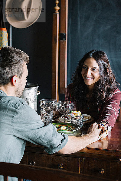 Romantisches junges Paar beim Essen  Hände über den Tisch haltend