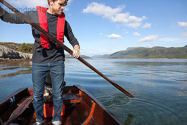 Reifer Mann steht auf  um das Ruder im Ruderboot zu benutzen  Aure  More og Romsdal  Norwegen
