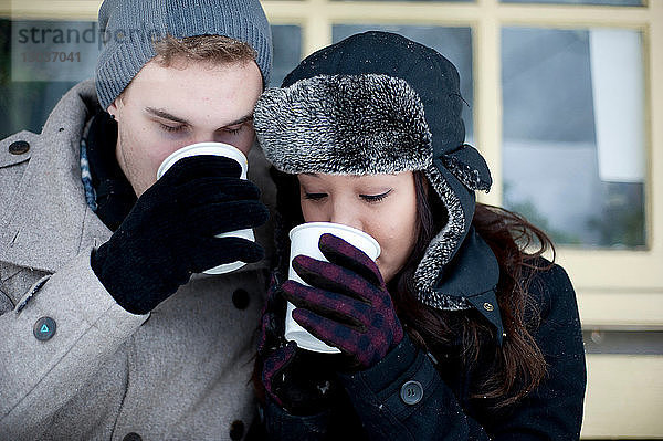 Junges Paar mit Winterhüten trinkt Kaffee zum Mitnehmen