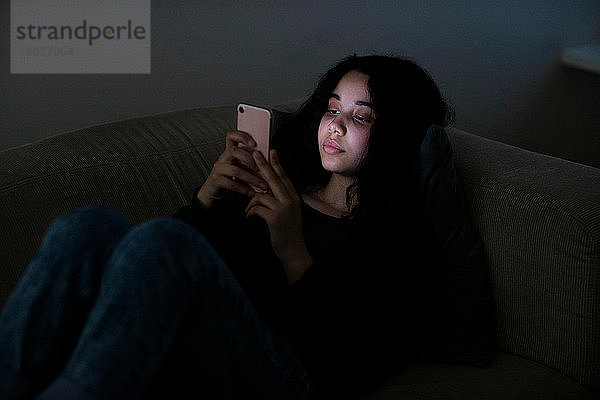 Teenager-Mädchen liegt im Dunkeln auf Sofa und liest SMS