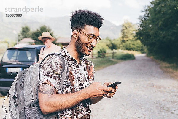 Junger männlicher Wanderer auf Feldweg mit Blick auf Smartphone    Primaluna  Trentino-Südtirol  Italien
