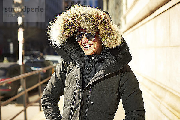 Taillenaufnahme einer lächelnden Frau in einer Winterjacke in der Stadt