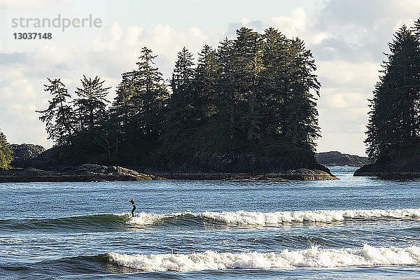 Fernblick auf einen einzelnen Surfer  der auf einer Welle im Meer reitet  Florencia-Bucht  Pacific Rim Park  Tofino  British Columbia  Kanada