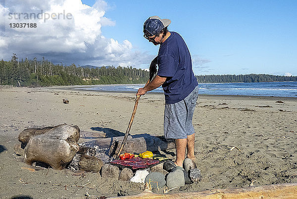 Mann  der am Strand über einem Lagerfeuer Essen zubereitet â€ Tofino  British Columbia  Kanada