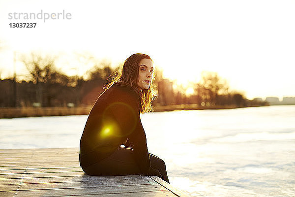 Seitenansicht einer einzelnen jungen Frau  die bei Sonnenuntergang auf einem Steg sitzt